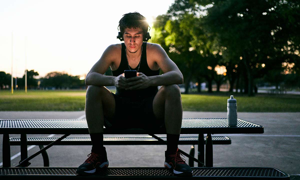Young man sitting on a park bench listening to music on phone