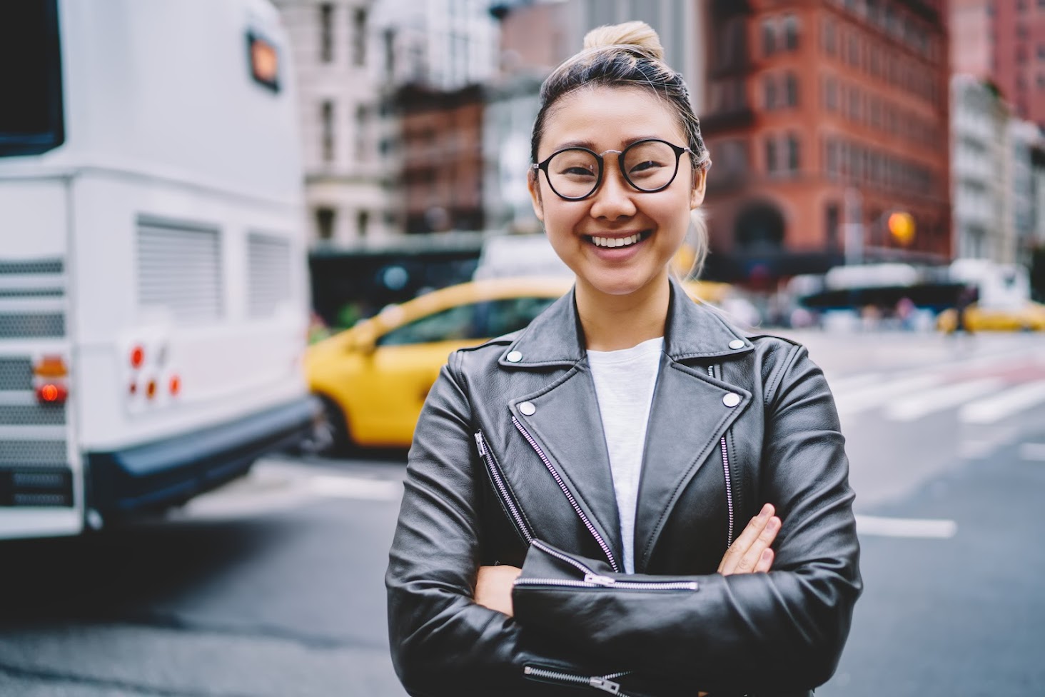 Young woman wearing glasses, standing in the city street smiling at camera