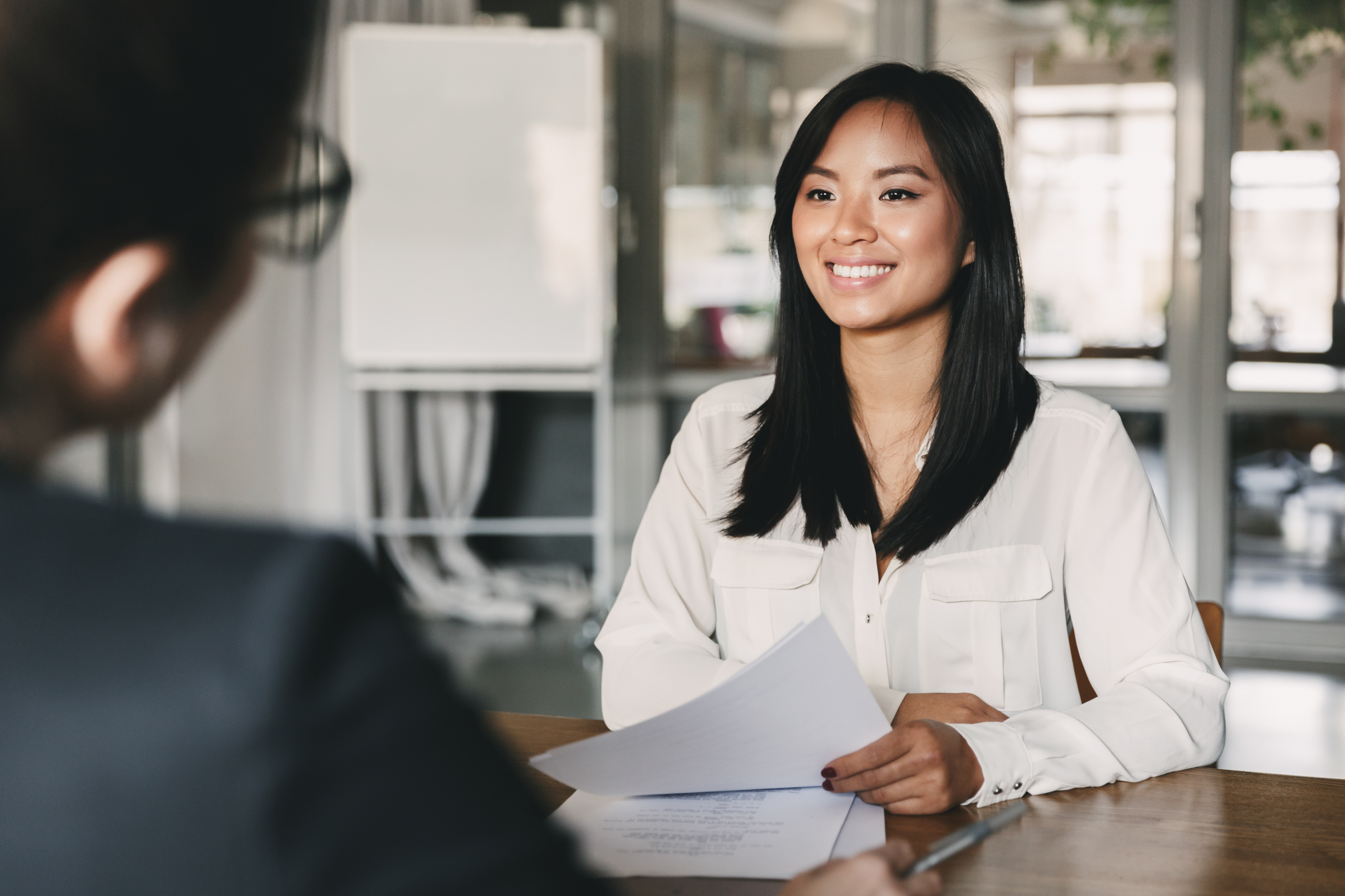 A woman smiling and holding papers while talking to a colleague in office.