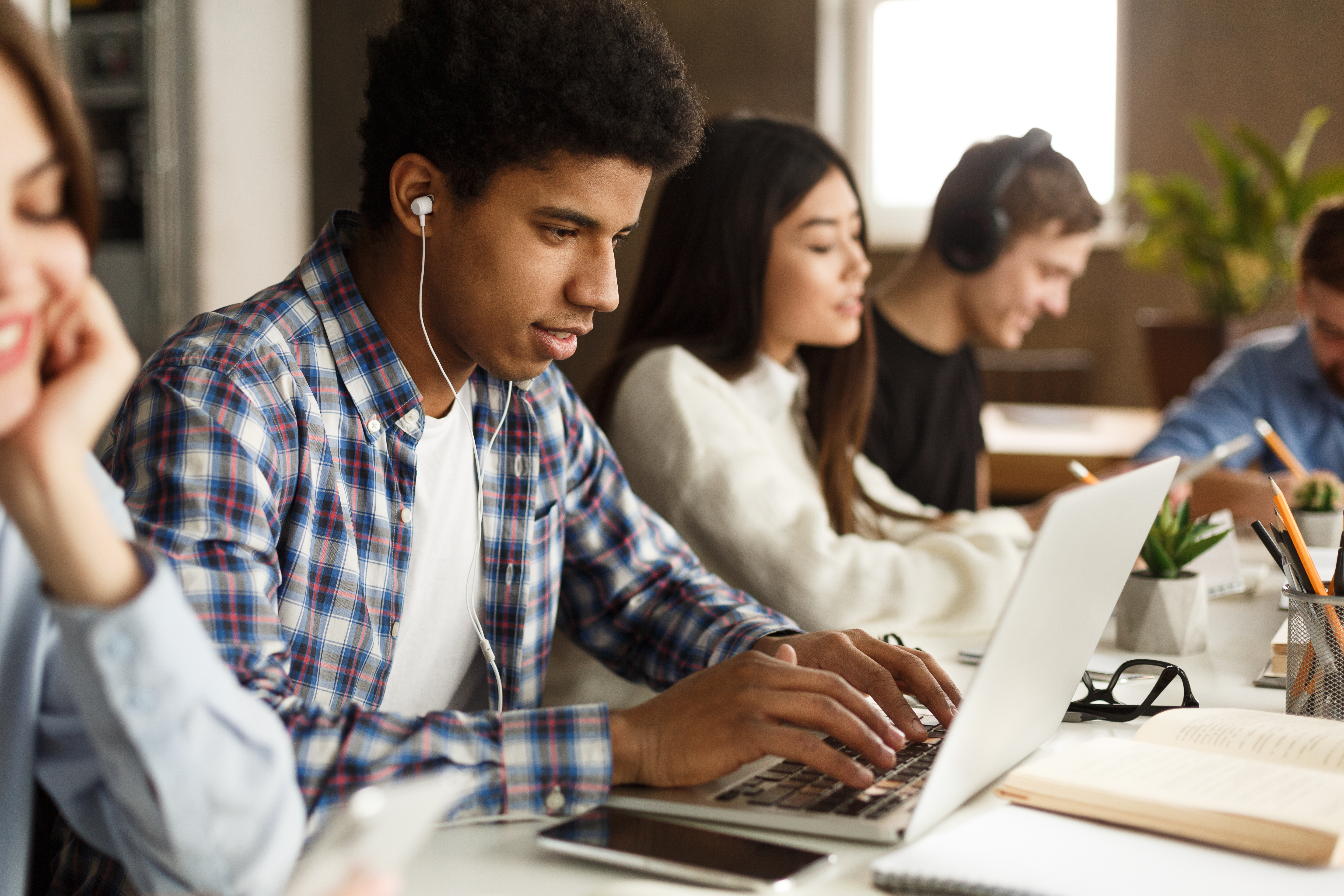 Young man in library with headphones in, working on computer.