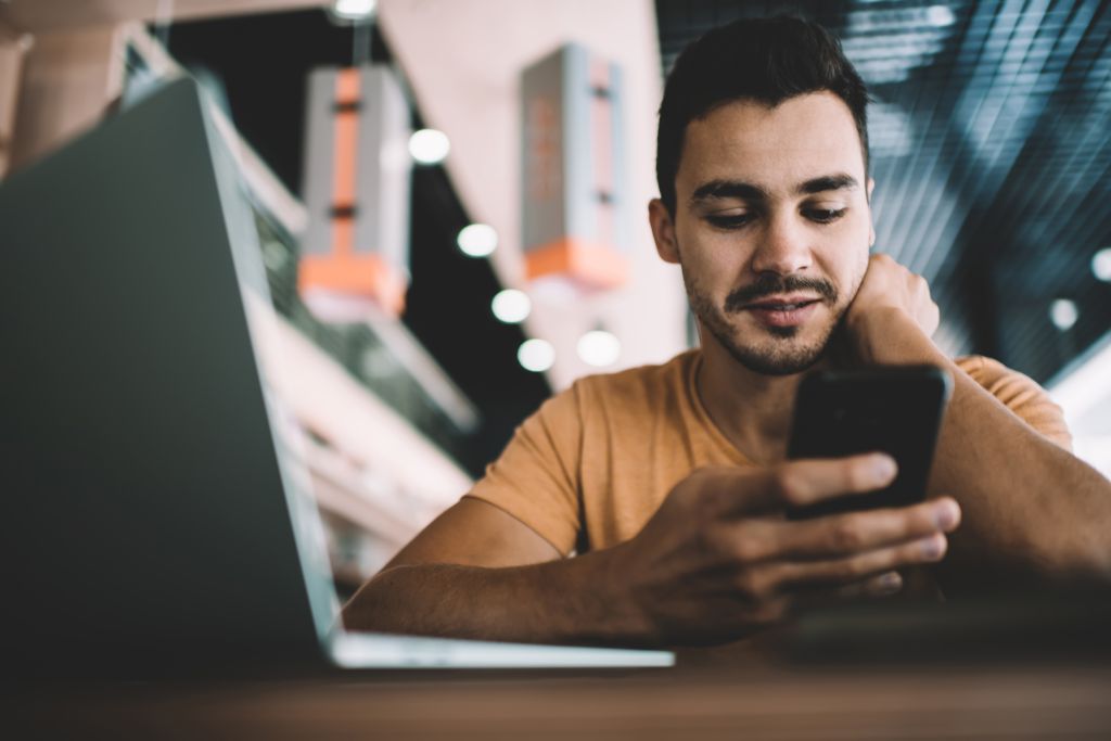 A young man looking at mobile phone's screen and reading.