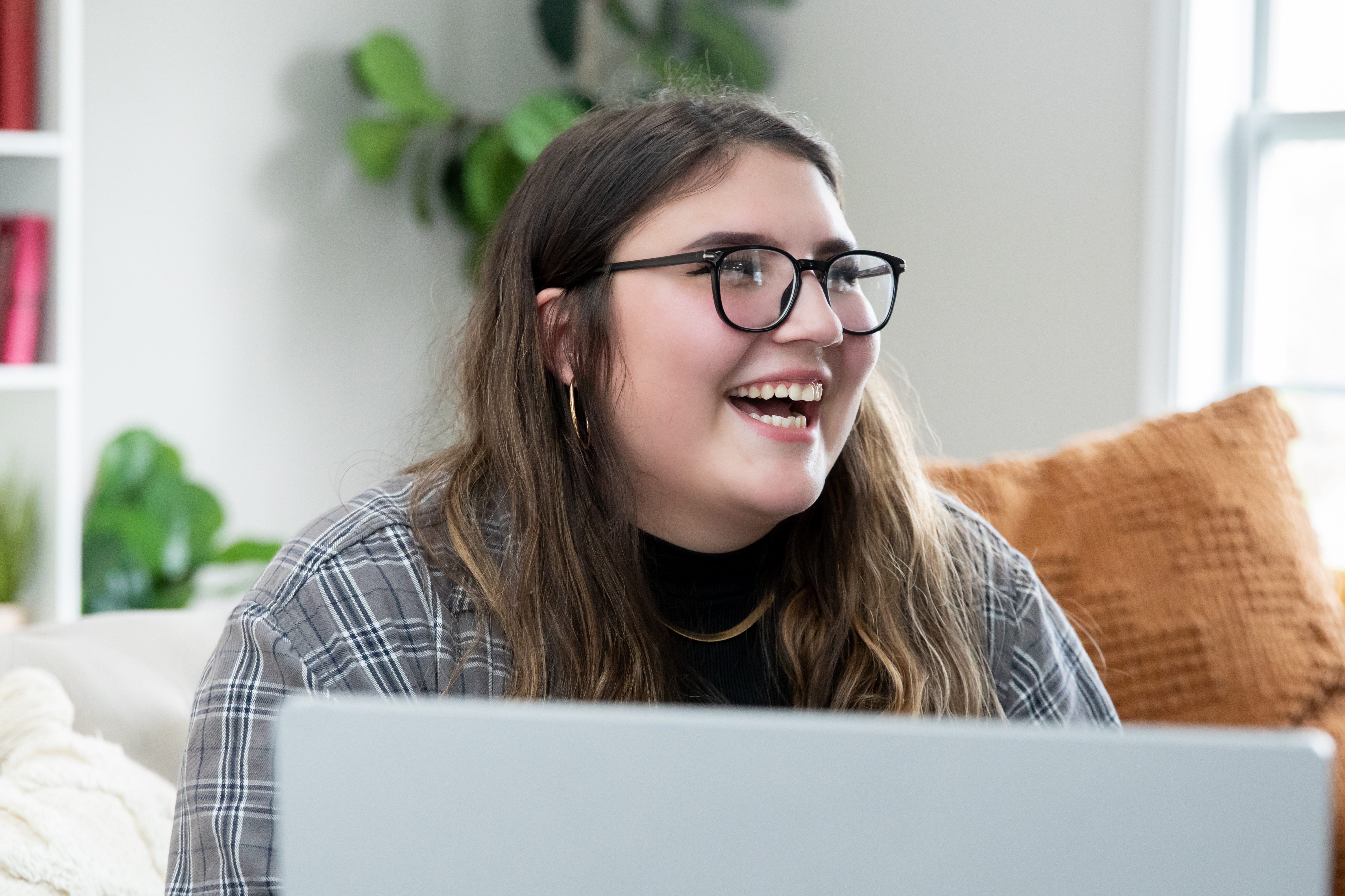 Indigenous youth on laptop at home smiling.