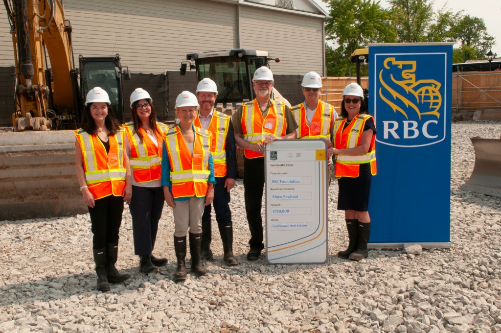 Des employés de RBC et du Festival Shaw, portant l’équipement de protection individuel de chantier, réunis sur le futur emplacement du réseau de puits géothermiques du festival.