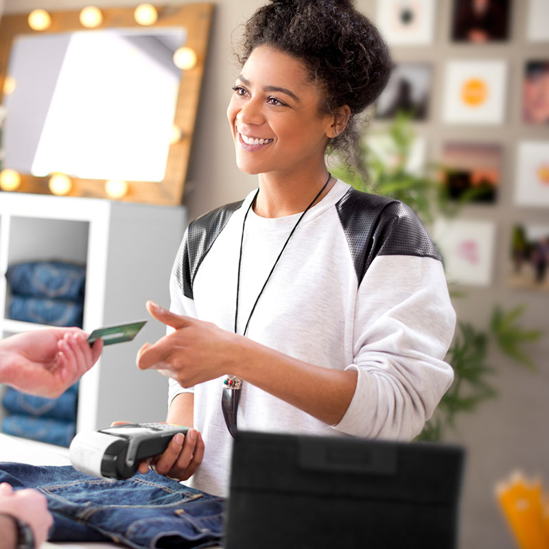 Vendeuse dans une boutique de vêtements acceptant la carte de crédit d’un client, un terminal au point de vente en main