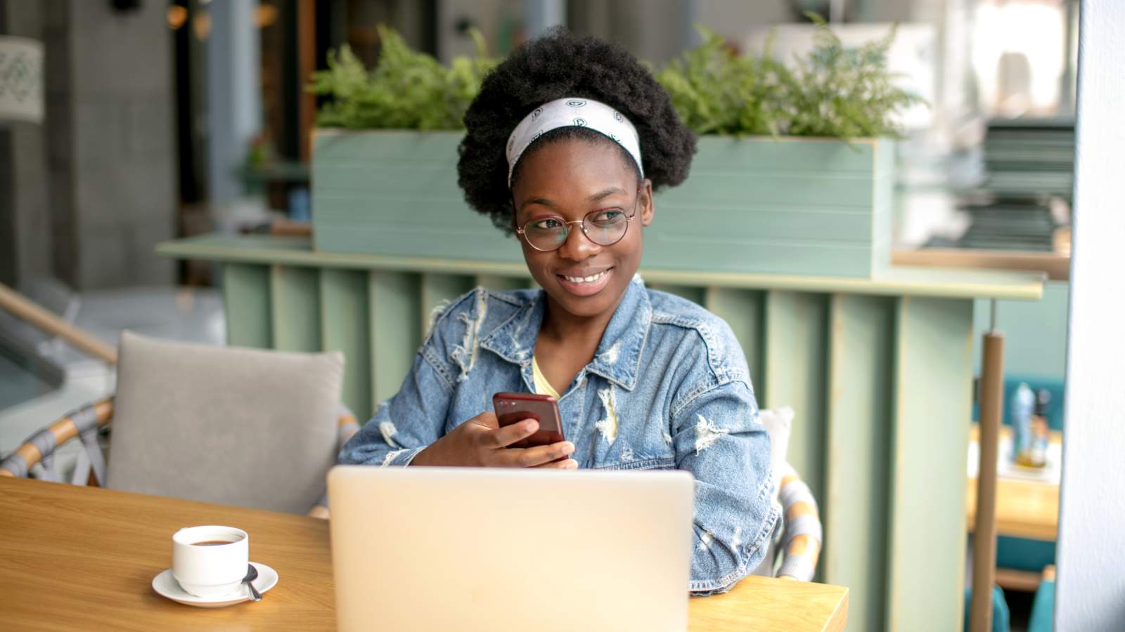 A young girl smiling and sitting by a coffee table with her phone and laptop